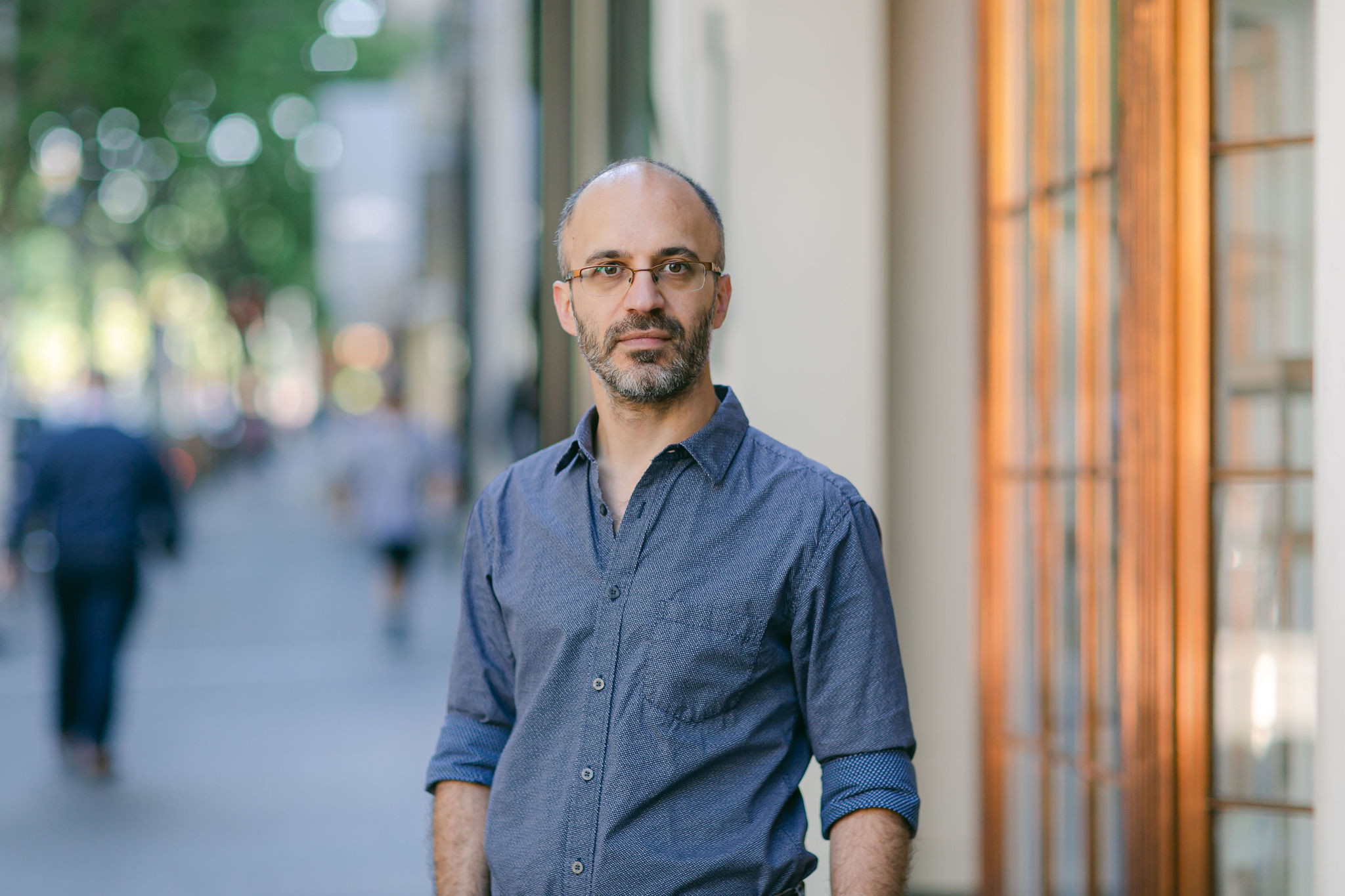 Dr Christos Symenoides standing outside a commercial building on a CBD street. He is wearing glasses and looks determined and trustworthy.